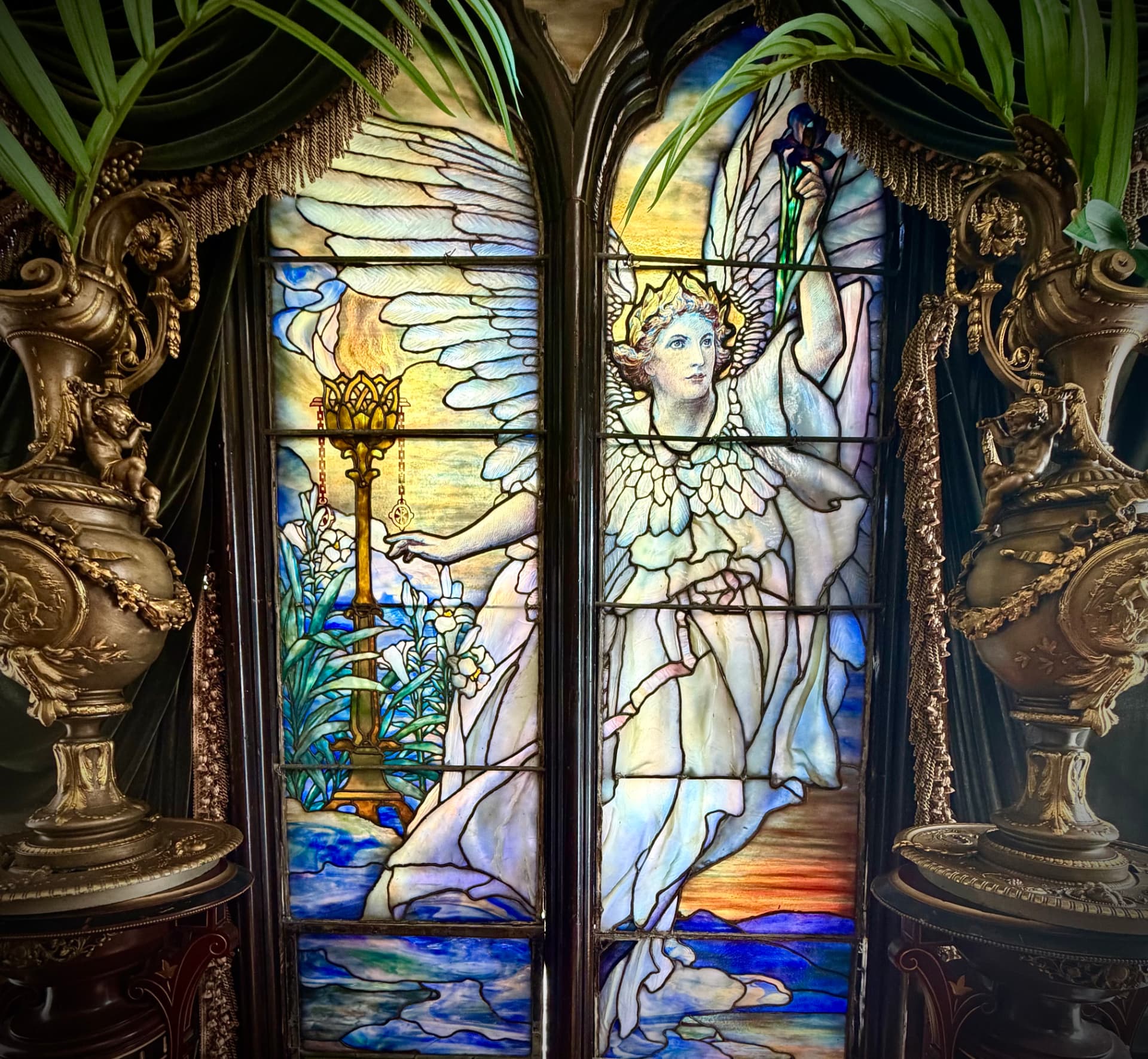 Historic Tiffany stained glass window with an angel, ornate lamp and palm fronds